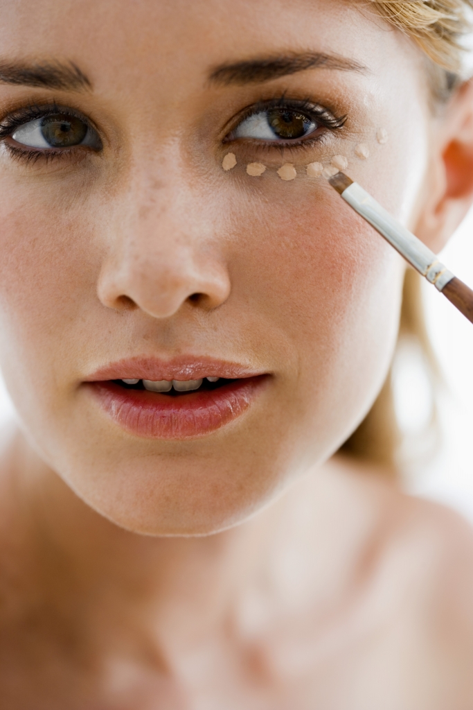 Woman with spots of makeup under her eye and makeup brush